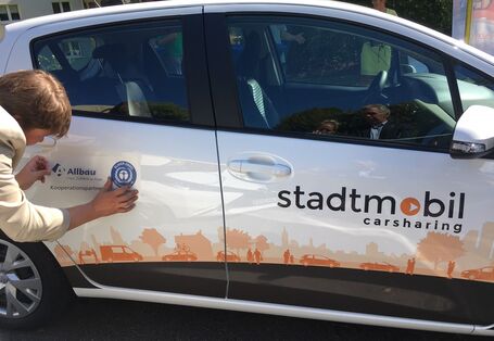 Aufkleber der Firma Allbau wird am Auto angebracht