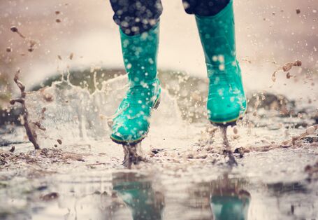 Kind springt mit Gummistiefeln in eine Pfütze