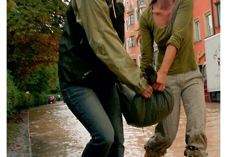 Cover von "Anpassung an den Klimawandel: Hochwasserschutz", Titelfoto: Zwei Frauen tragen gemeinsam einen Sandsack durch eine überflutete Straße