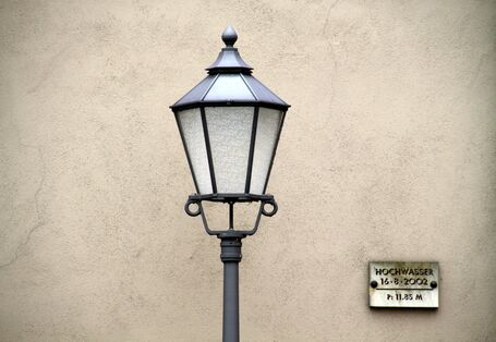 Straßenlaterne vor einer Mauer, an der auf gleicher Höhe eine Hochwassermarkierung angebracht ist