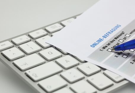 Tastatur auf der ein Blatt Papier liegt, auf dem erste Fragen einer Befragung zu erkennen sind