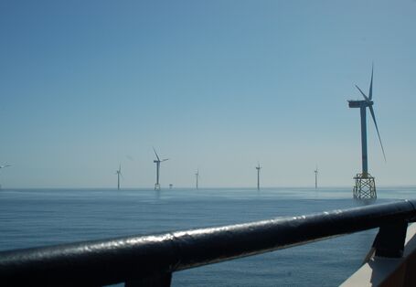 Das Foto zeigt den Blick von einem Schiff auf den Offshore-Windpark Alpha Ventus. Im Vordergrund sieht man Windenergieanlagen mit Jacket-Fundamenten (als Fachwerk konstruierte Gründungsstrukturen) und im Hintergrund mit Monopile-Fundamenten