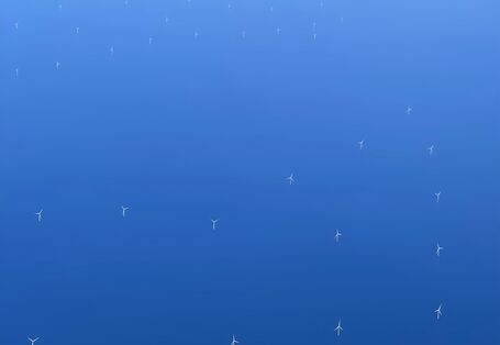Das Foto zeigt eine Luftaufnahme von Offshore Windenergieanlagen. Man sieht einzelne Windenergieanlagen aus dem Meer herausragen.