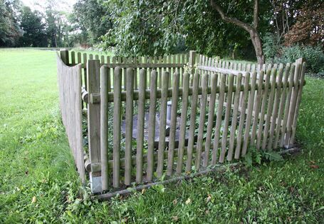 Umzäunter Brunnen mit Holzlatten auf grüner Wiese in Großaufnahme.