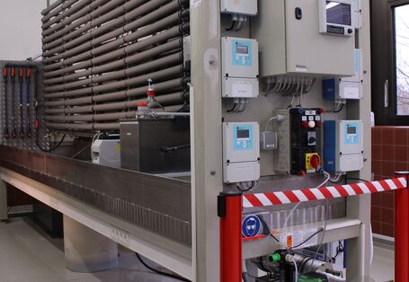 Teststand für Desinfektionsmittel. Im Vordergrund rechts elektronische Schalt- und Steuereinheiten, im Hintergrund links wärmeisolierte Wasserrohre der Teststrecke.