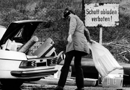 ein Mann lädt an einem Schild "Schutt abladen verboten" Müll aus seinem Autokofferraum aus