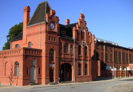 Small, old red-brick train station building with spire and gable