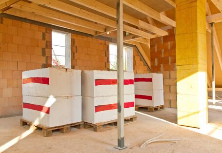 ein Gebäude im Rohbau von innen, auf Paletten stehen Baumaterialien