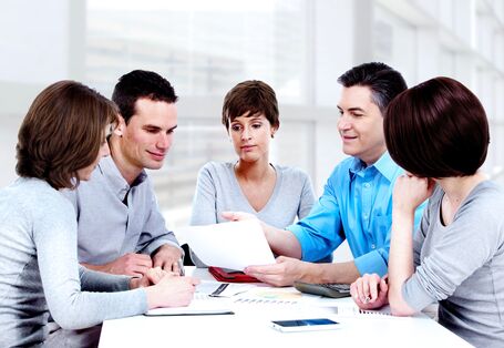 Zwei Männer und drei Frauen sitzen an einem Tisch in einem Büro zu einer Besprechung 