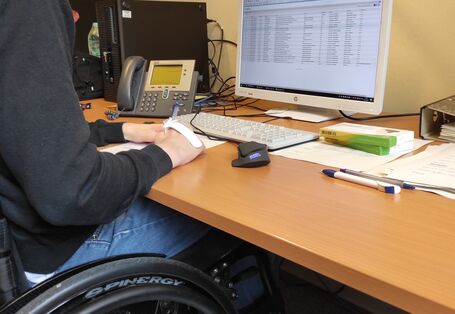 ein junger Mann sitzt im Rollstuhl im Büro an einem Schreibtisch 