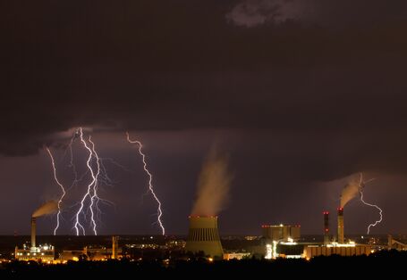 über einer Industrieanlage bei Nacht tobt ein Unwetter mit Blitzen und dunklen Wolken