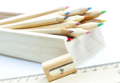 unlackierte Holz-Buntstifte in einem Holzkästchen, daneben ein Anspitzer aus Holz und ein Lineal