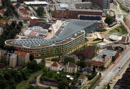  The UBA building in Dessau-Roßlau from above. The building is elongated, with a façade of wood and coloured glass slabs and slanted solar cells covering the entire surface of the flat roof
