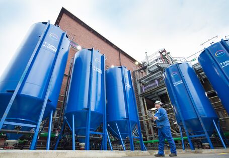 Mann in Arbeitskleidung vor 5 riesigen blauen Tanks vor einer Werkhalle