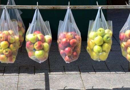 an einer Eisenstange über einem gepflasterten Platz oder Fußweg hängen durchsichtige Plastiktüten mit Äpfeln