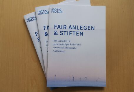 drei Druckversionen des Leitfadens "Fair anlegen & stiften", auf dem Cover sind Windkraftanlagen abgebildet