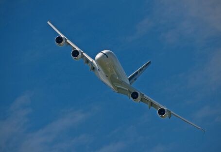 fliegendes Flugzeug mit vier Triebwerken vor blauem Himmel