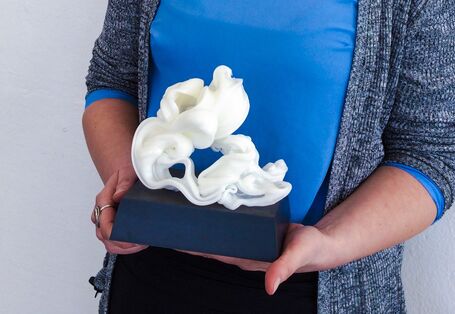 junge Frau mit einer Trophäe in der Hand, ein weißes, filigranes Gebilde auf einem Sockel