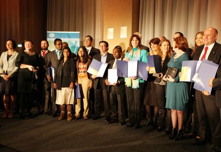 etwa 20 Männer und Frauen stehen für ein Foto aufgereiht auf einer Bühne