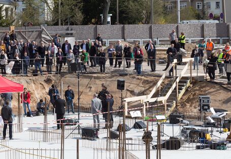 Blick von oben auf eine betonierte Bodenplatte, auf der ein Fest gefeiert wird. Viele Gäste stehen am Rand der Baustelle.