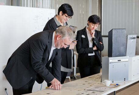 ein Mann und zwei Frauen schauen sich auf einem Tisch liegende Gegenstände und Ausdrucke an.