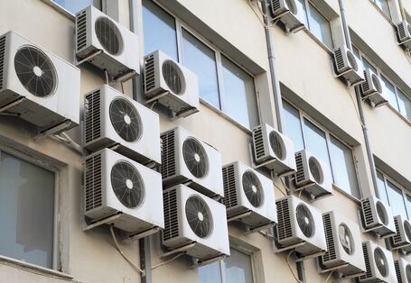 außen an einer Hauswand hängen viele Klimageräte