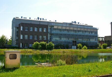 Modern three-storey, elongated office building, with river or canal with grassy banks at the front