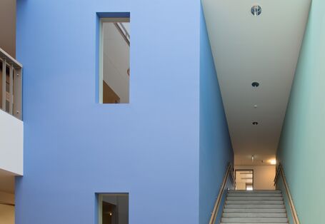 kleine Eingangshalle mit Glasdach und Treppenaufstieg, die Wände sind weiß, die Wände des Treppenhauses jedoch links blau uns rechts hellgrün gestrichen