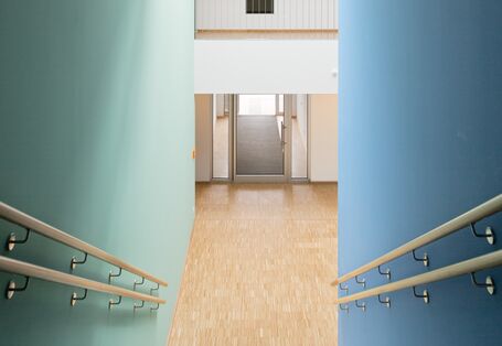 Treppe abwärts mit Holz-Handläufen, die rechts Wand ist blau, die linke in einem hellen grün-blau gestrichen