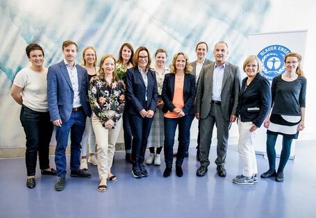 Neun Frauen und drei Männer haben sich vor einer Stellwand mit dem Logo "Blauer Engel" zu einem Gruppenfoto aufgestellt