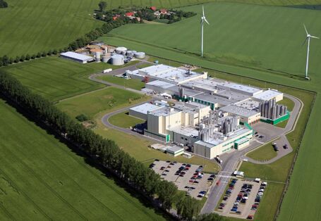 Firmengelände mit mehreren Gebäuden, Tanks und einem Parkplatz inmitten von Feldern