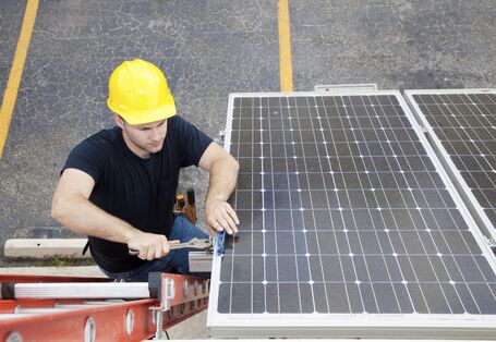 ein Mann mit Bauhelm steht auf einer Leiter und montiert eine Photovoltaikanlage