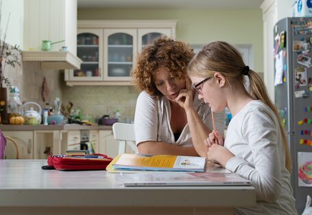 Mutter und Tochter sitzen am Küchentisch über einem Lehrbuch