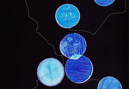 runde, blaugefärbte Stoffstücke mit einem Faden verbunden vor schwarzem Hintergrund