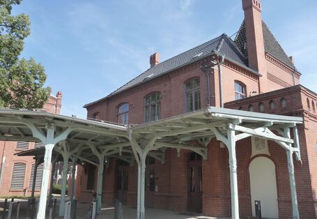 kleines Bahnhofsgebäude aus Backstein, davor ein grau gestrichenes Holz-Vordach