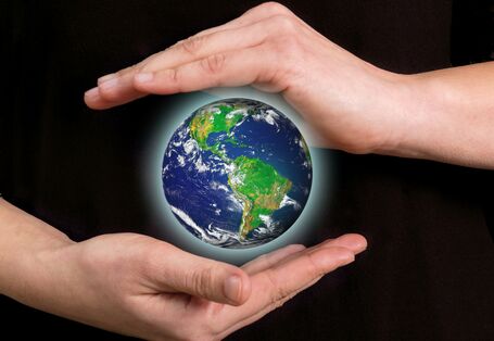 ein Mensch hält schützend seine Hände über und unter eine schwebende und leuchtende Erdkugel