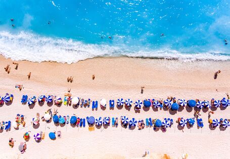 Menschen an einem Meeresstrand mit Sonnenschirmen von oben
