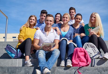 eine Gruppe Studentinnen und Studenten sitzt mit Rucksäcken und Schreibblöcken auf einer Steintreppe