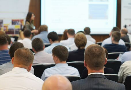 Besucher eines Vortrags mit Präsentation sitzen in Reihen
