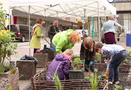 Kinder und Erwachsene bepflanzen Hochbeete und Blumenkübel in der Stadt