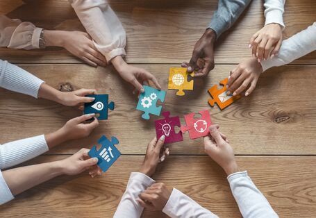 Hände verschiedener Menschen, die bunte Puzzleteile mit verschiedenen Symbolen aneinander fügen