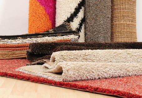 mehrere Teppiche auf einem Haufen, dahinter stehen Teppich-Rollen