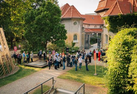 Vor dem ehemaligen Krematorium öffnet sich eine Grünfläche, auf der sich TeilnehmerInnen austauschen.