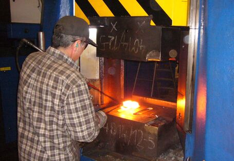 Mann arbeitet an einem glühenden Metallteil in einer Schmiedemaschine