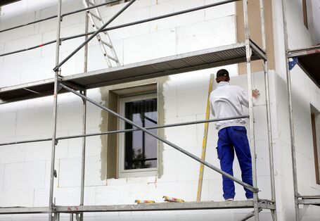 Handwerker steht auf einem Baugerüst und bringt Styroporplatten an eine Hausfassade an