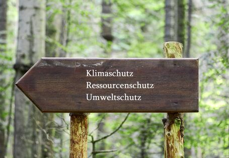 auf einem hölzernen Wegweiser im Wald stehen die Worte Klimaschutz, Ressourcenschutz und Umweltschutz