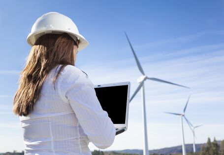 Ingenieurin steht mit Laptop und Bauhelm vor einem Windpark