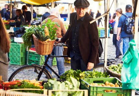 ein Mann kauft mit dem Fahrrad Gemüse auf einem Wochenmarkt ein