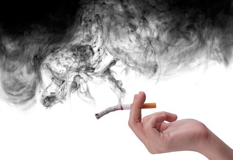 Hand hält eine schon halb zu Asche gewordene Zigarette, von der schwarzer Qualm aufsteigt