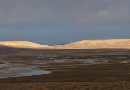 Arktische Landschaft: Die Sonne scheint auf einen Fluss und sanfte braune Hügel.